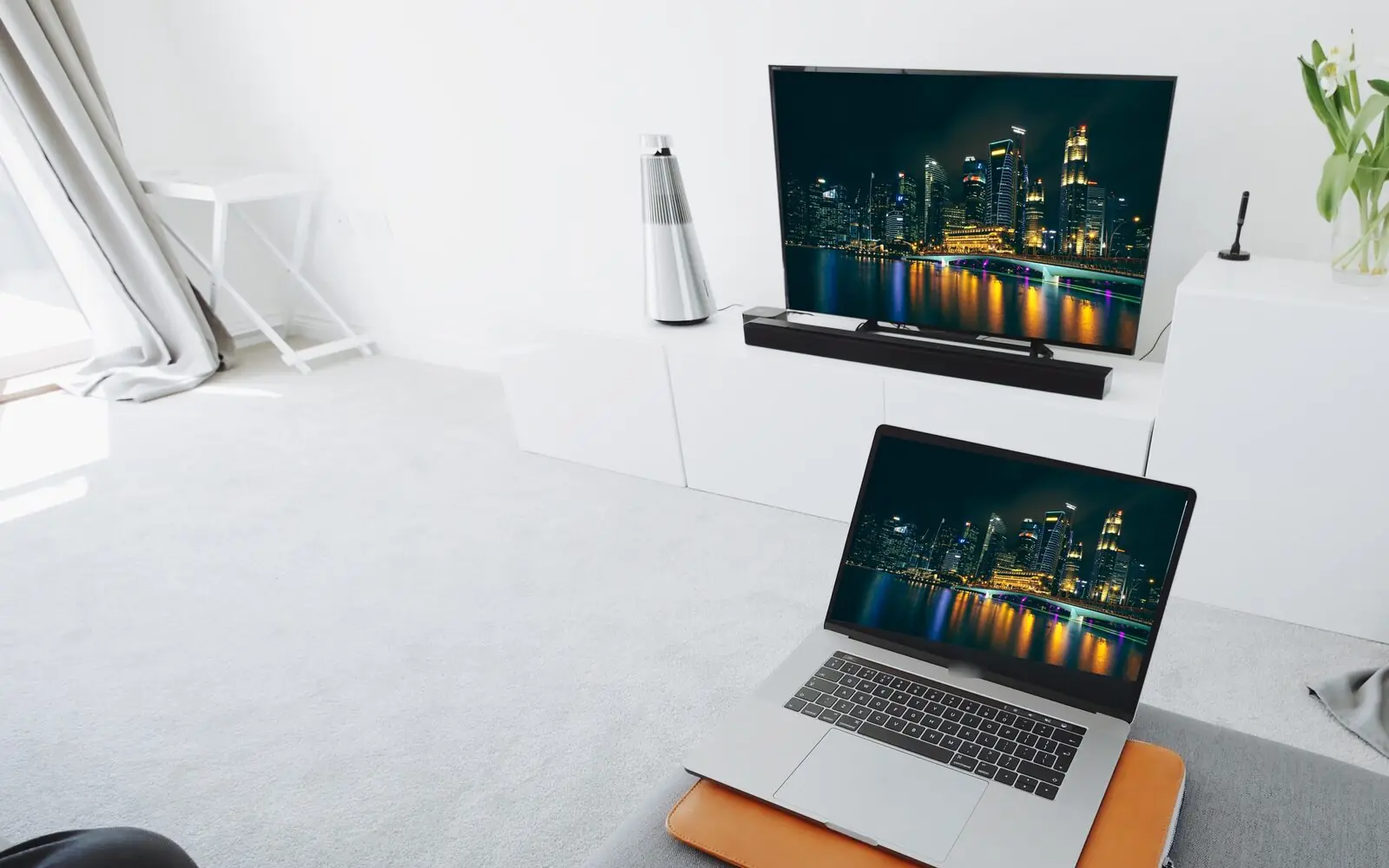 Living room with a TV and a laptop both showing the Singapore skyline at night